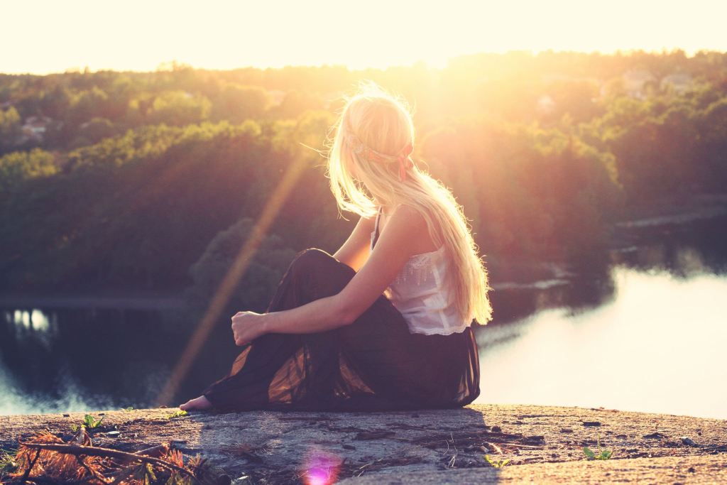 Woman sitting on a rock overlooking water.